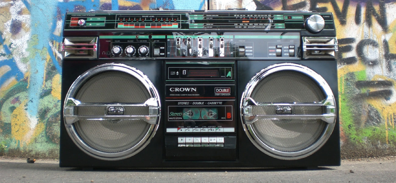 A boom box stereo sitting on the ground next to a grafitted wall.