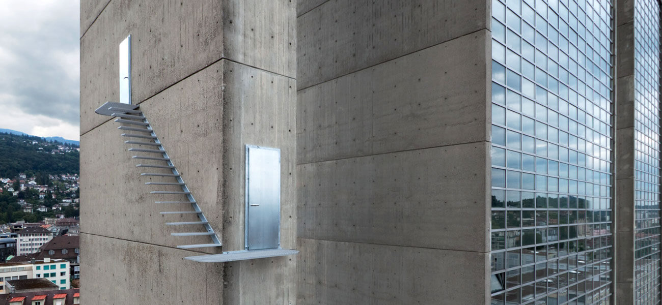 A staircase emerges half-way up a skyscraper, turns a corner, then enters a second door.