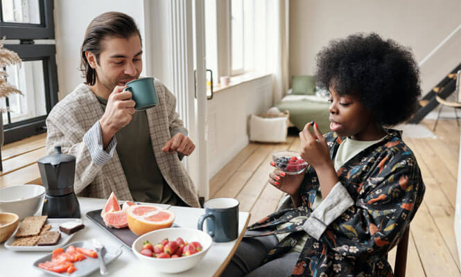 A couple eat a simple meal of fruit in a white appartment.