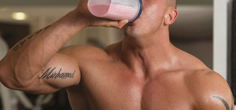 A man drinks a bright pink liquid in a gym.