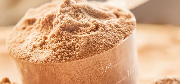A measuring cup sitting inside a tub of brown powder.