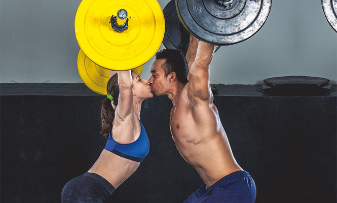 A couple kiss while weightlifting.